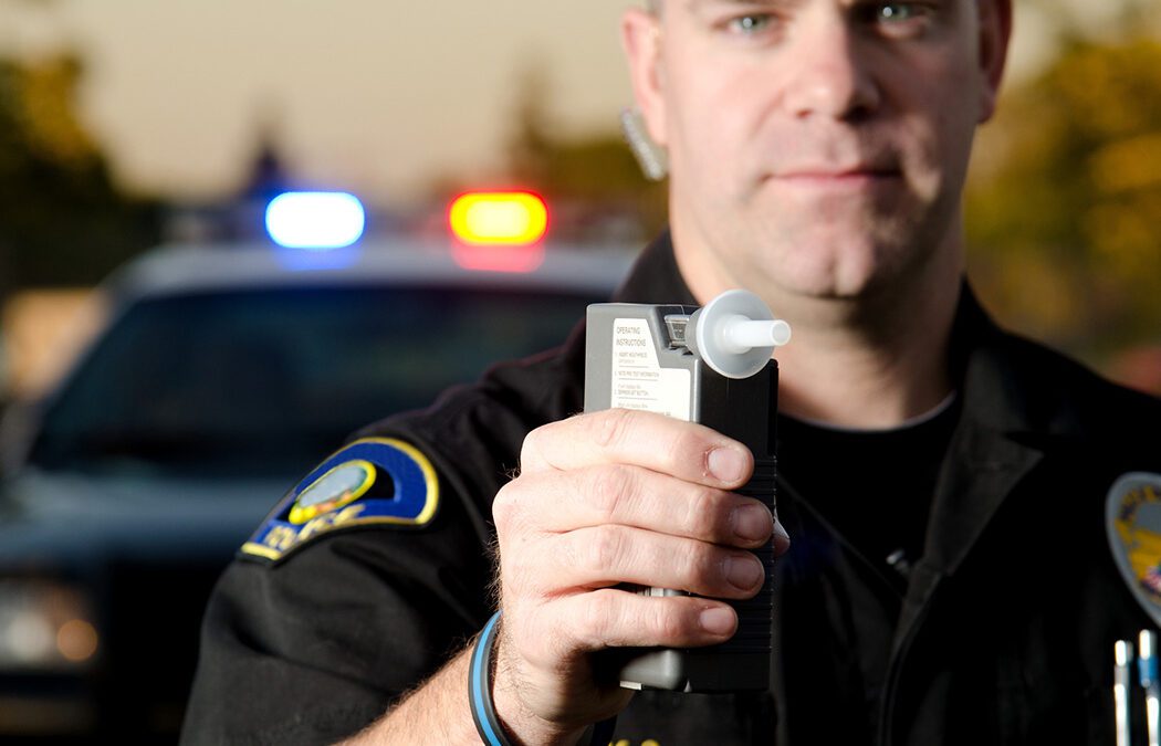 A police officer holds a breath test machine in his hand ready at a traffic stop with his patrol car in the background.*the officer was blurred on purpose to place focus on the mouth piece.